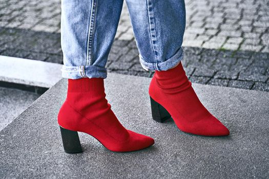 Woman legs in red sexy trendy knitted fabric block heel sock boots shoes and blue denim jeans pants on grey tiles background