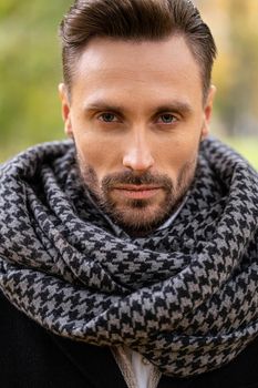 Handsome young man in dark blue coat and scarf or muffler. A young business man stands on the street in an autumn coat looks confidently at the camera.