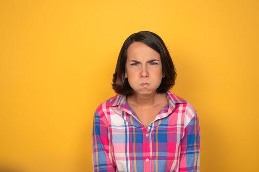 Making funny faces pretty looking girl looking to camera. Woman in a plaid shirt on yellow background. Human emotions, facial expression concept.