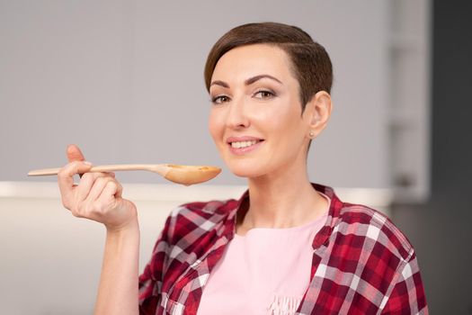 Young housewife with a short hairstyle testing a food while prepares dinner for family in the kitchen. Healthy food at home. Healthy food leaving - vegan concept.