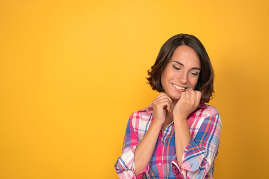 Charming woman expressing tenderness and saying good bye in plaid shirt on a yellow background with copy space. Facial expressions, emotions, feelings.