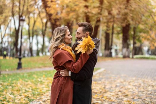 About a kiss shot. Husband and a wife hugged smile looking at each other in the autumn park. Outdoor shot of a young couple in love having great time having a hug in a autumn park.