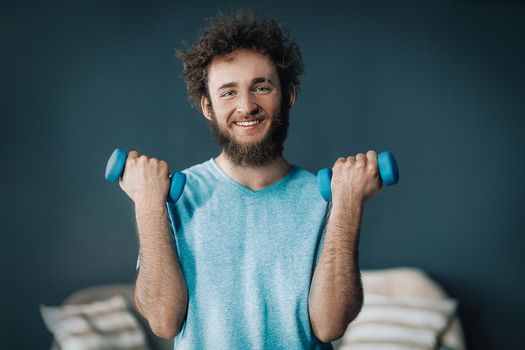 Handsome Man Does Fitness with Dumbbells At Home. Guy Keeps Fit During Quarantine. Gray background. High quality photo