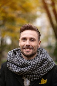 A happy young man standing on the street in an autumn coat smiling at his girlfriend or wife looking at the camera. Handsome young man in dark blue coat and scarf or muffler.