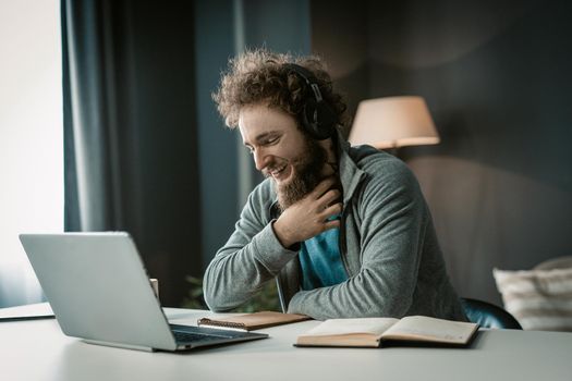 Young Teacher has an Online Video Conference Lesson with his Students During the Distance Learning Due to Quarantine. Man with Headphones sits at his Desk and Looks into the Screen of his Laptop. Close-up . High quality photo