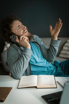 Caucasian Guy has an Emotional Conversation on his Mobile Phone. Diary and Laptop are on the Desktop. Close-up. High quality photo