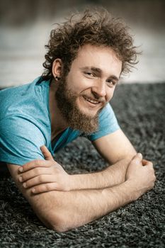 Attractive Caucasian Guy in a Blue T-shirt Relaxed on the Carpet. Smiling Man Resting on the Carpet After Funny Party. Close-up . High quality photo