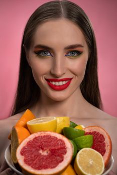 Beauty fashion model girl with beautiful make up, red lips, long healthy hair and bawl of colorful fresh cut citrus fruits in her hands. Lime, orange, lemon, grapefruit. Fashion concept.