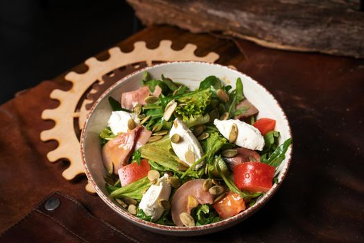 Fresh Vegan Salad with Vegetables, Fish, Cheese, Egg, Pumpkin Seeds, Arugula in White Ceramic Bowl on a Leather Apron. Top view. High quality photo