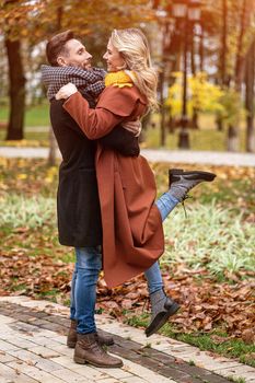 Husband lifting a wife hugged laughing in the autumn park with a cute hug. Outdoor shot of a young couple in love having great time having a hug in a autumn park. Tinted image.