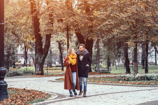 A married couple is walking in the autumn park with a cute hug. Outdoor shot of a young couple in love walking along a path through a autumn park. Tinted image.
