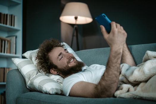 Shapely Guy Watches his Favorite Serials on his phone before going to sleep. He watches serials the whole night in his bed. Close-up. High quality photo