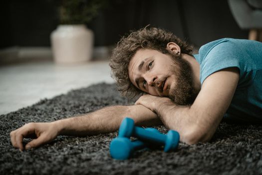Exhausted Man After a Hard Workout Lies Tired on the Floor Next to Dumbbells. Lazy Guy Doesn't Want to Do Sports, Lack of Energy. Close-up. High quality photo