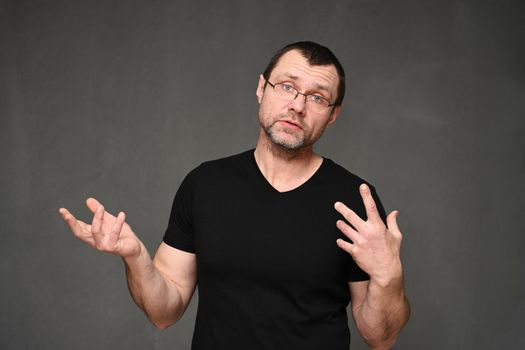 Caucasian man in a black t-shirt with glasses talking with emotions on a gray background