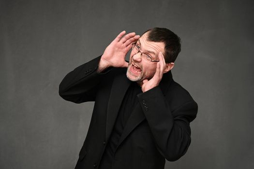 Caucasian man in a black jacket with glasses shouting to the side with emotions on a gray background
