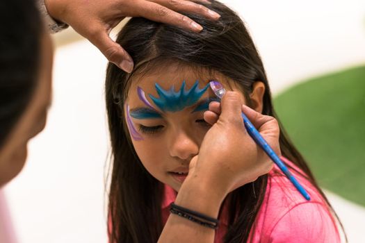 Girl painting her face like a princess by face painting artist