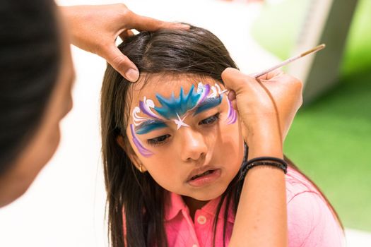 Girl painting her face like a princess by face painting artist