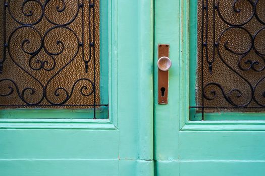 Old turquoise Mediterranean style vintage door with handle, keyhole and glass parts with forged figured lattices