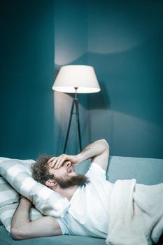 Caucasian Guy Wants to Sleep But Cannot Because of Noisy Neighbors. Tired Man Lies in His Bed and Yawns. Close-up. Bedroom Background. High quality photo