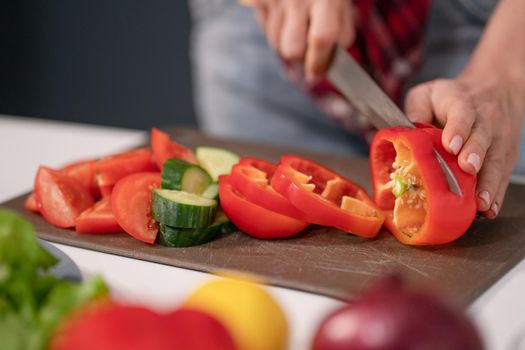 Woman cutting sweet pepper or bell pepper using knife on plastic cut board. Freshly cut vegetables for fresh salad. Healthy leaving concept. Raw food concept.