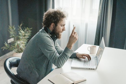 Young Businessman Analyzes New Online Business Strategies During the Quarantine Period. Young Man Sitting at the Table With a Cup of Coffee and Typing Text on His Laptop. Close-up. High quality photo