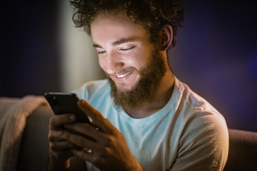 Curly Guy Swipes on His Phone Sitting on the Couch. Nice Man is Typing a Message to His Girlfriend on His Phone. Close up portrait. High quality photo