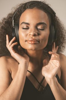 Close up. Capture away by music young African-American girl listening music with eyes closed wearing headphones, isolated on grey background, emotionally move, have fun.