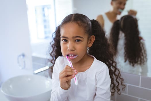 Portrait of biracial girl brushing teeth with reflection of father in mirror in background. unaltered, family, love and togetherness concept.