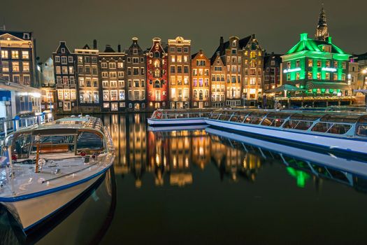 Traditonal houses and cruise boats at the Damrak in Amsterdam in the Netherlands by night