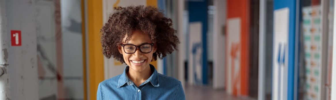 Happy Afro American woman in glasses standing in the hallway while holding paper box, copy space