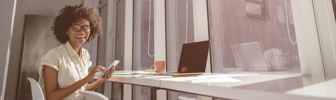 Happy pretty woman sitting at work desk and working with laptop while holding mobile phone