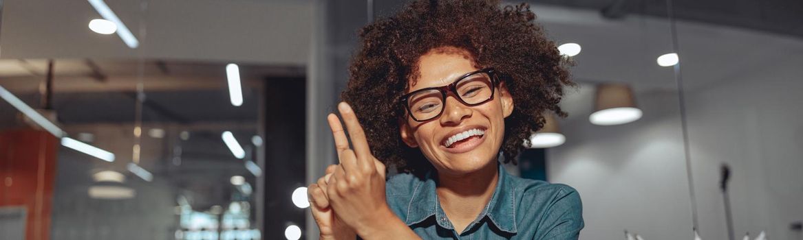 Smiling African American lady talking with sign language while sitting at her workplace in the office