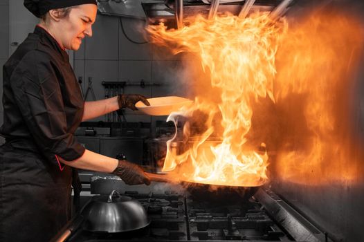 Woman Chef Cooking wok in the Kitchen. Cooking flaming wok with vegetables in the commercial kitchen. High quality photography.