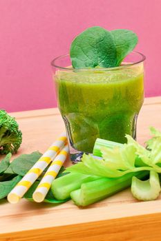 Fresh Green Smoothie of Apple, Celery, and Spinach in Glass Beaker with Yellow Cocktail Straw on Wooden Cutting Board. Vegan Detox Drink. Vegetarian Culture. Healthy Eating and Fruit Diet