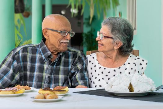 Elderly couple wearing glasses sitting at a table, both are smiling