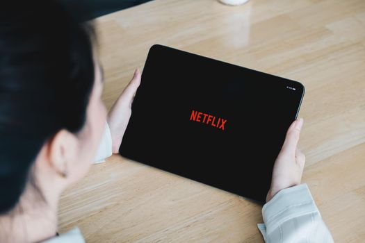 CHIANG MAI, THAILAND, JULY 26, 2020: Woman hand holding Smart tablet with Netflix logo on Apple iPad. Netflix is a global provider of streaming movies and TV series.