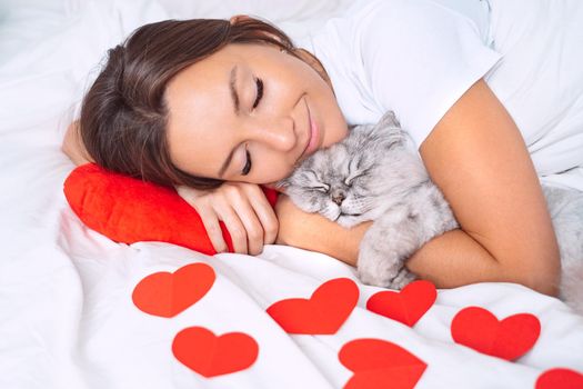 Woman lying on the bed with red hearts and hugging her lovely cat. Love for pets. High quality photo