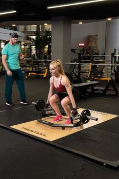 RUSSIA, MOSCOW - FEB 11, 2022: Instructor and client girl deadlift blonde trap bar trainer teach, in the afternoon instructions motivation in healthy for sport trap, eadlift couple. Assisting female weight, active