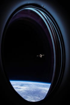 View on ISS Progress resupply ship, View out from a passenger window on the SpaceX Crew Dragon. Docking maneuver near the Space Station. Elements of image furnished by NASA.