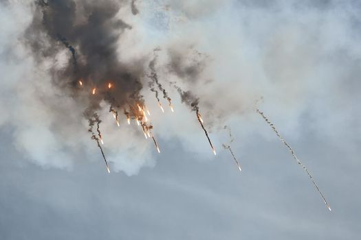 Aircraft fighter flies and shoots heat guns in the blue sky. Fighter shoots off heat traps during the maneuver. A fighter during a demonstration aerobatics.