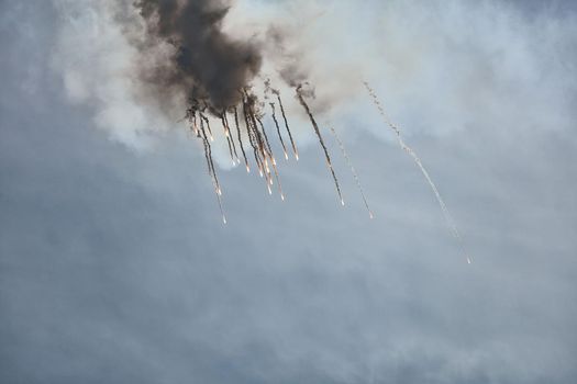 Aircraft fighter flies and shoots heat guns in the blue sky. Fighter shoots off heat traps during the maneuver. A fighter during a demonstration aerobatics.