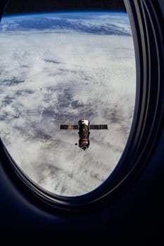 View on ISS Progress resupply ship, View out from a passenger window on the SpaceX Crew Dragon. Docking maneuver near the Space Station. Elements of image furnished by NASA.