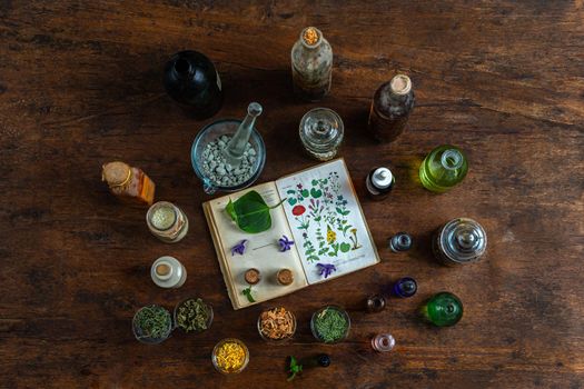 Old book on plants, surrounded by dried herbs, essential oils, salts, in vitage containers