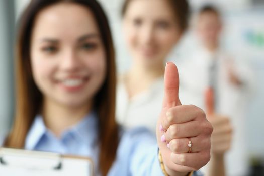 Close-up of smiling female showing thumbs up and confirm success on camera. Business partners posing in company office. Business, goal, good job concept