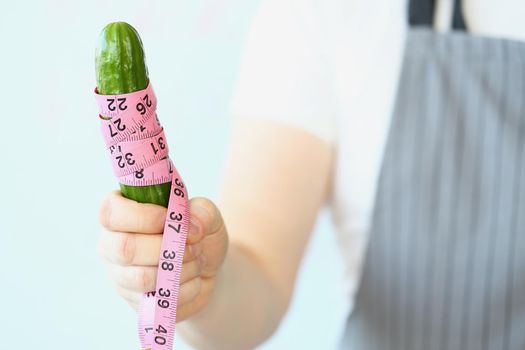 Close-up of person hold cucumber with measure tape around, diet and healthy and organic food. Sport nutrition for slim figure. Healthy lifestyle concept