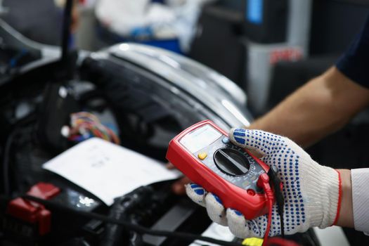 Close-up of mechanics hand hold multimeter equipment to measure voltage of automobile battery. Worker provide inspection of car. Garage service concept