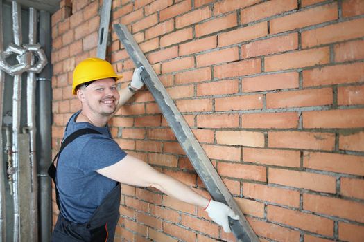 Portrait of happy constructor hold metal detail close to brick wall, concrete red wall in empty room. Creating house, building process. Renovation concept