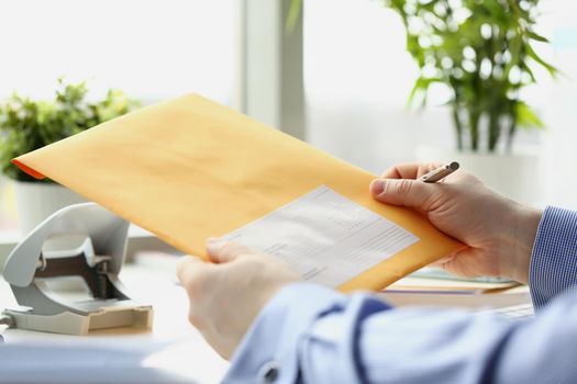 Close-up of man holding yellow envelope and going to fill in personal address on cover. Answer to correspondence, check letters. Delivery service concept