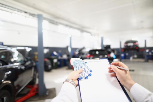 Close-up of male worker fill maintenance documentation, view on car garage. Professional handyman work in garage. Car service, pit stop, vehicle concept