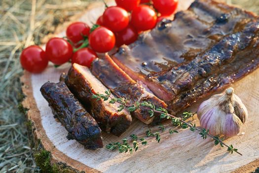 Barbecue ribs meat prepared in traditional European style with rosemary herb cherry tomatoes and garlic on a raw solid wood cutting plate